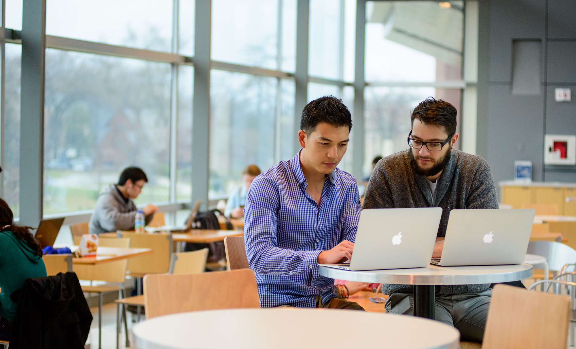 Two students working together on laptops in a study lounge